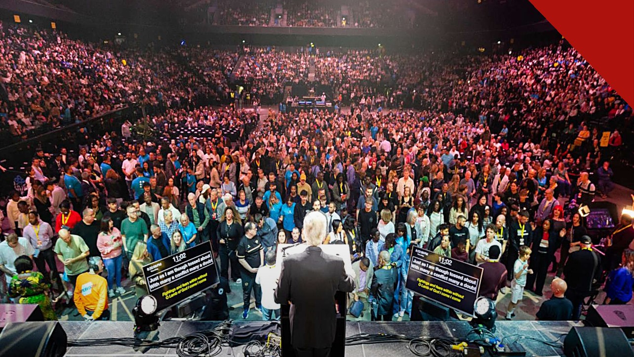 Franklin Graham vê sinais de avivamento: o evangelista de costas no púlpito diante de mais de 10 mil pessoas na arena de Manchester, na turnê God Loves You