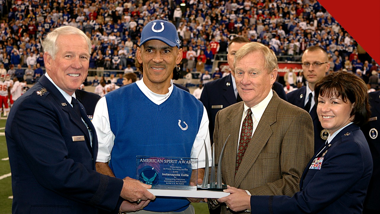 Tony Dungy repreende pastor que defende poligamia, e a imagem mostra Tony Dungy, de colete azul do Indianapolis Colts, recebendo uma homenagem em campo, cercado por oficiais e convidados