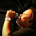 Tasha Cobbs Leonard anuncia Unscripted Christmas: cantora em perfil cantando ao microfone em apresentação ao vivo