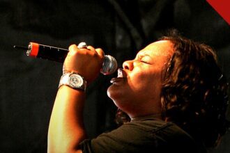 Tasha Cobbs Leonard anuncia Unscripted Christmas: cantora em perfil cantando ao microfone em apresentação ao vivo