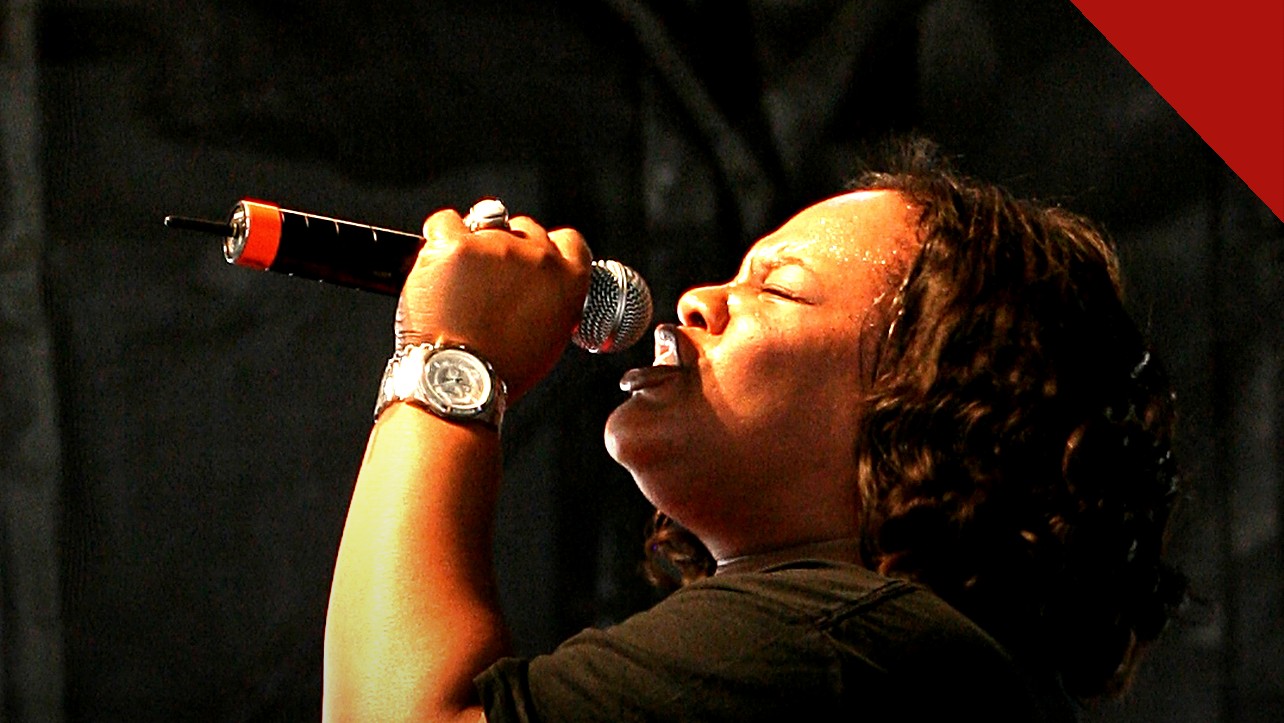 Tasha Cobbs Leonard anuncia Unscripted Christmas: cantora em perfil cantando ao microfone em apresentação ao vivo