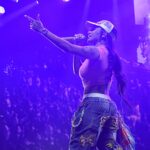 GloRilla recria clipe de Ciara e Bow Wow: GloRilla canta em palco com luz roxa, microfone na mão e braço levantado, em foto de apresentação ao vivo