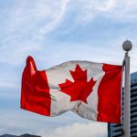 Samuel Sey é removido dos Estados Unidos para o Canadá, e a imagem mostra a bandeira do Canadá tremulando em um mastro no Canada Place, em Vancouver, com prédios de vidro ao fundo e céu azul