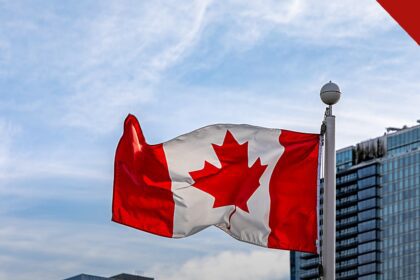 Samuel Sey é removido dos Estados Unidos para o Canadá, e a imagem mostra a bandeira do Canadá tremulando em um mastro no Canada Place, em Vancouver, com prédios de vidro ao fundo e céu azul