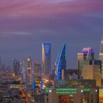 Estados Unidos retiram funcionários da Arábia Saudita, e a imagem mostra o horizonte de Riade, capital da Arábia Saudita, ao entardecer, com torres iluminadas como a Kingdom Tower e a Al Faisaliah, cidade onde fica a embaixada americana