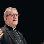O bispo Barron critica academia alemã: o bispo Robert Barron falando em palestra, de batina preta e cruz peitoral