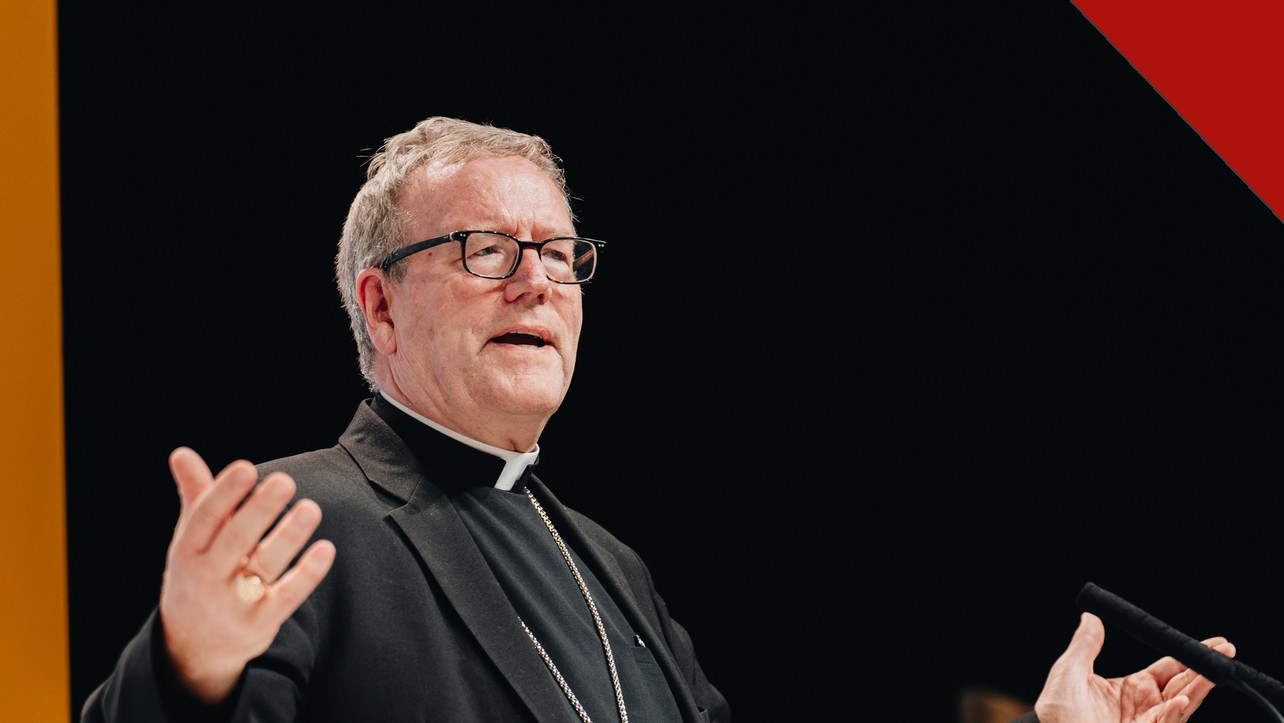 O bispo Barron critica academia alemã: o bispo Robert Barron falando em palestra, de batina preta e cruz peitoral