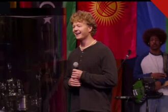 Missionário Jonathan sorri ao compartilhar o testemunho durante o mês de missões da Calvary Christian Church, com bandeiras das nações ao fundo
