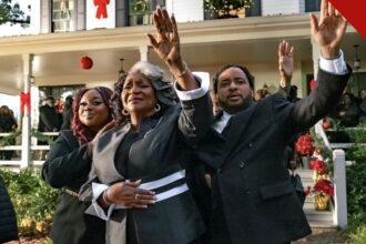 Cena do filme de Natal de Tyler Perry, The Gospel of Christmas, com fiéis de mãos levantadas diante de casa decorada para o Natal