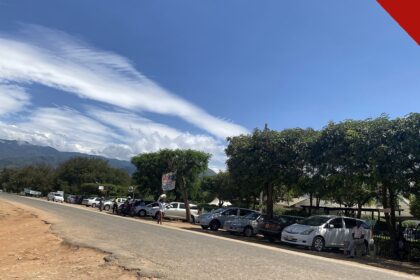 Vista de rua em Kasese, distrito do cristão morto em Uganda, Benjamin Kule Mayani, com carros estacionados, árvores e montanhas ao fundo