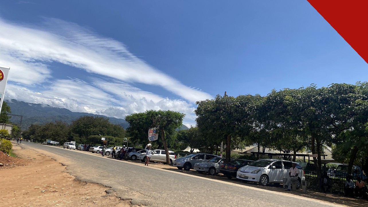 Vista de rua em Kasese, distrito do cristão morto em Uganda, Benjamin Kule Mayani, com carros estacionados, árvores e montanhas ao fundo