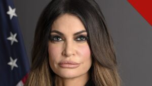 Retrato oficial de Kimberly Guilfoyle, embaixadora dos Estados Unidos na Grécia, diante da bandeira americana