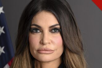 Retrato oficial de Kimberly Guilfoyle, embaixadora dos Estados Unidos na Grécia, diante da bandeira americana
