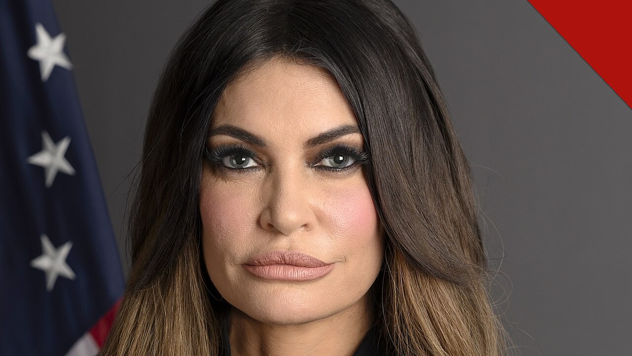 Retrato oficial de Kimberly Guilfoyle, embaixadora dos Estados Unidos na Grécia, diante da bandeira americana