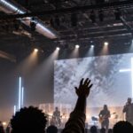 Fiéis de igrejas negras dos Estados Unidos em culto com banda de worship, telão de LED e cruz iluminada ao fundo