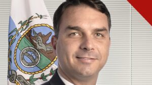 Flávio Bolsonaro, de terno escuro e gravata clara, em retrato oficial do Senado, com a bandeira do Rio de Janeiro ao fundo