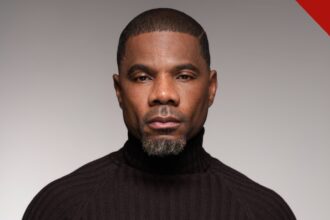 Kirk Franklin em retrato de estúdio com gola preta, olhando para a câmera