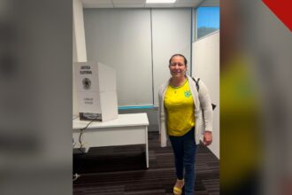 primeira pessoa a votar no segundo turno: Luziene Alves ao lado da cabina de votação na Embaixada do Brasil em Wellington