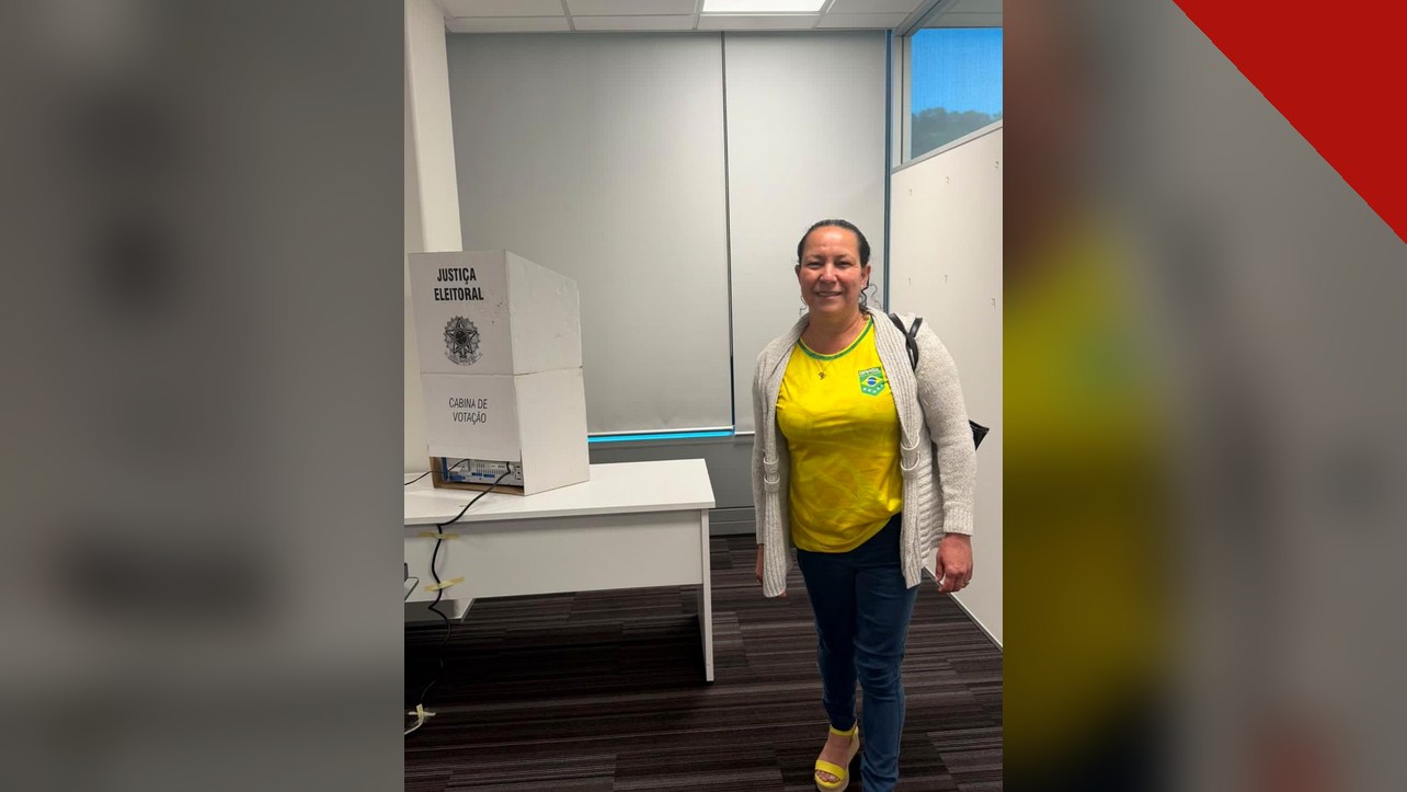 primeira pessoa a votar no segundo turno: Luziene Alves ao lado da cabina de votação na Embaixada do Brasil em Wellington