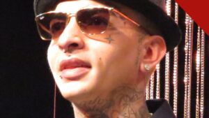 MC Guimê, de chapéu e óculos escuros, com as tatuagens do rosto e do pescoço à mostra, em retrato de 2015