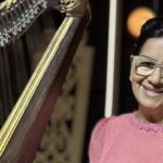 morre Sara Araújo: a cantora gospel pioneira sorrindo ao lado de uma harpa, de vestido rosa