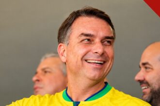 Flávio Bolsonaro fora do Brasil é o relato atribuído a aliados pela CNN Brasil, e a imagem mostra o senador Flávio Bolsonaro sorrindo com a camisa da seleção brasileira