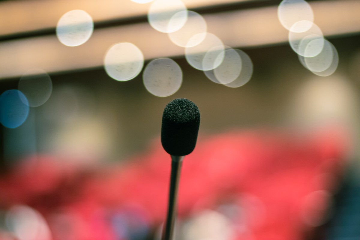 MC Guimê anuncia transição para o gospel diante da plateia do show de despedida, e a imagem mostra um microfone em púlpito sob luzes de palco desfocadas, em foto ilustrativa de arquivo