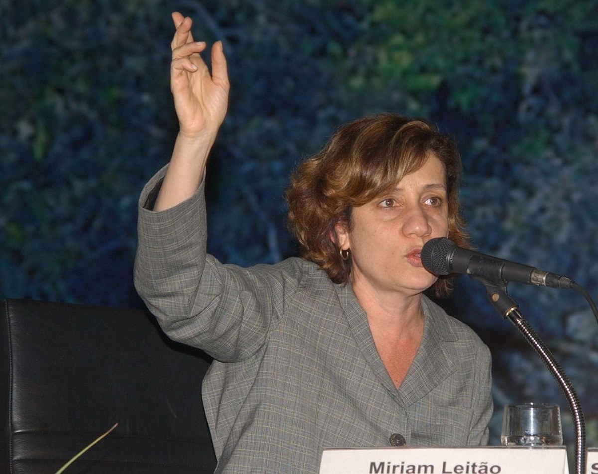Miriam Leitão passa mal ao vivo na GloboNews, e a imagem mostra a jornalista Miriam Leitão falando a um microfone em evento, em foto de arquivo